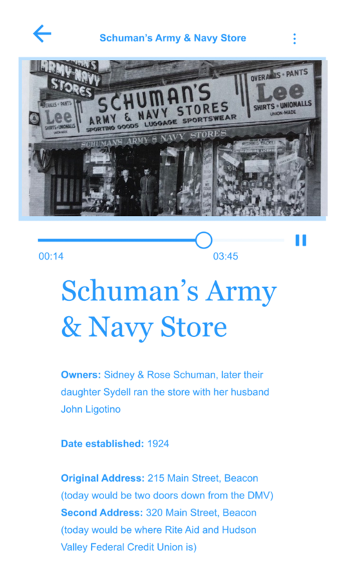 A screenshot of a sample business card for the Jewish Beacon Walking Tour phone app. There is sky blue text on a white background. A black and white photo of Schuman’s store is on the screen on top, and an audio player is seen underneath it. The title reads “Schuman’s Army & Navy Stores” and the text underneath gives information about the business. 